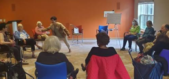 An improv facilitator leading an interactive activity with residents seated in a circle