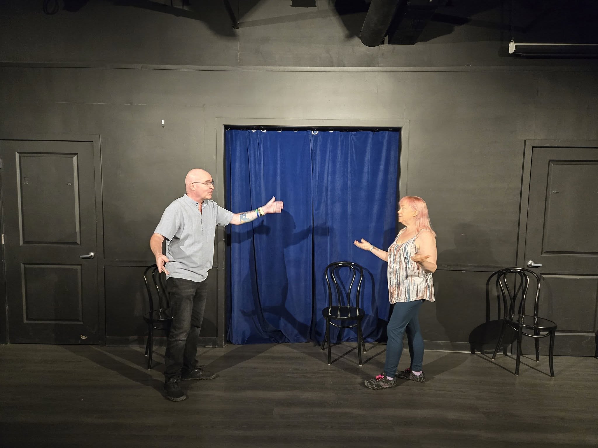 Daniel and Chan performing an improv scene on stage, gesturing toward each other