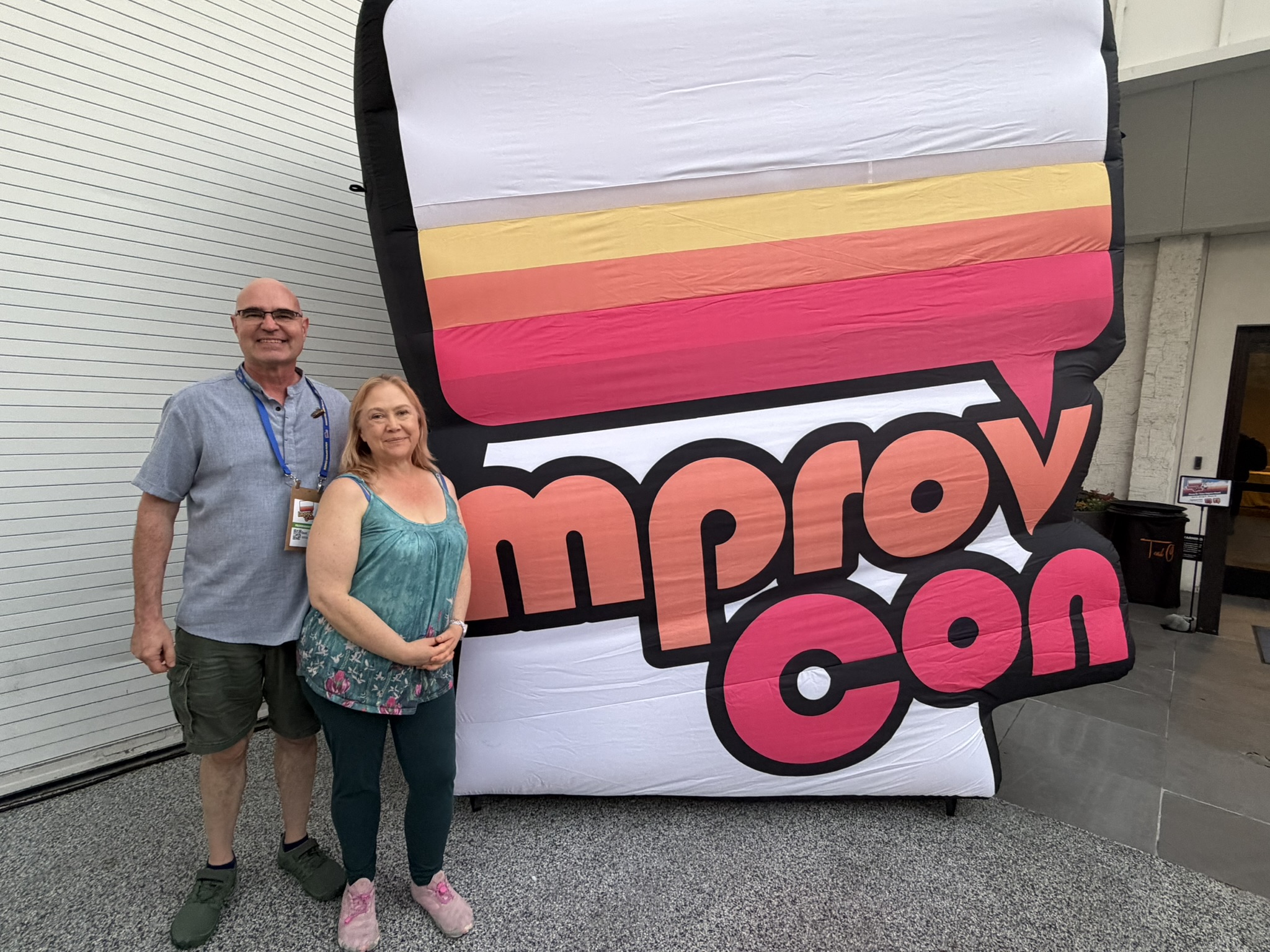 Daniel and Chan standing together in front of the ImprovCon sign